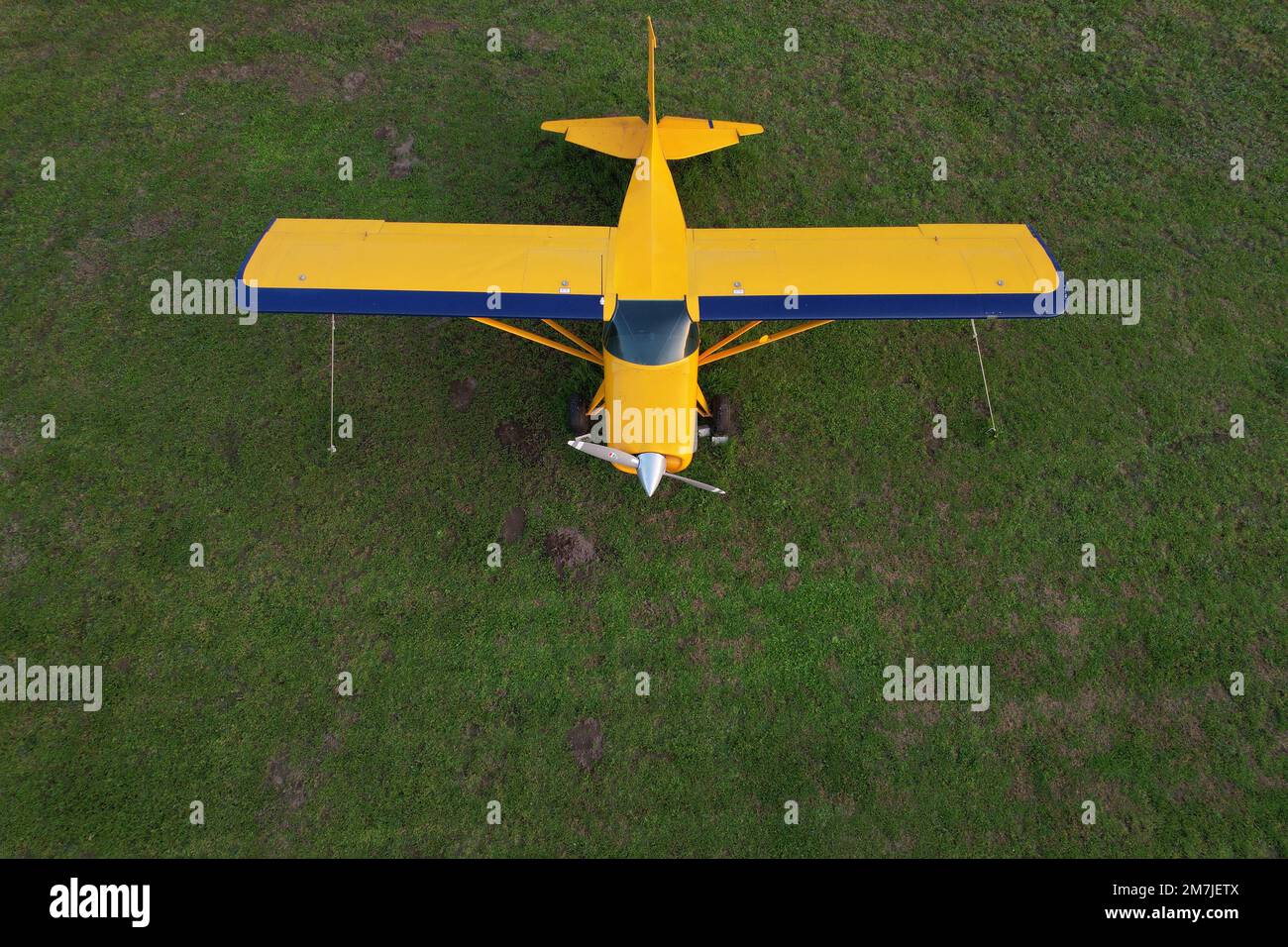 small yellow plane used for short trips seen from above parked on a green field Stock Photo