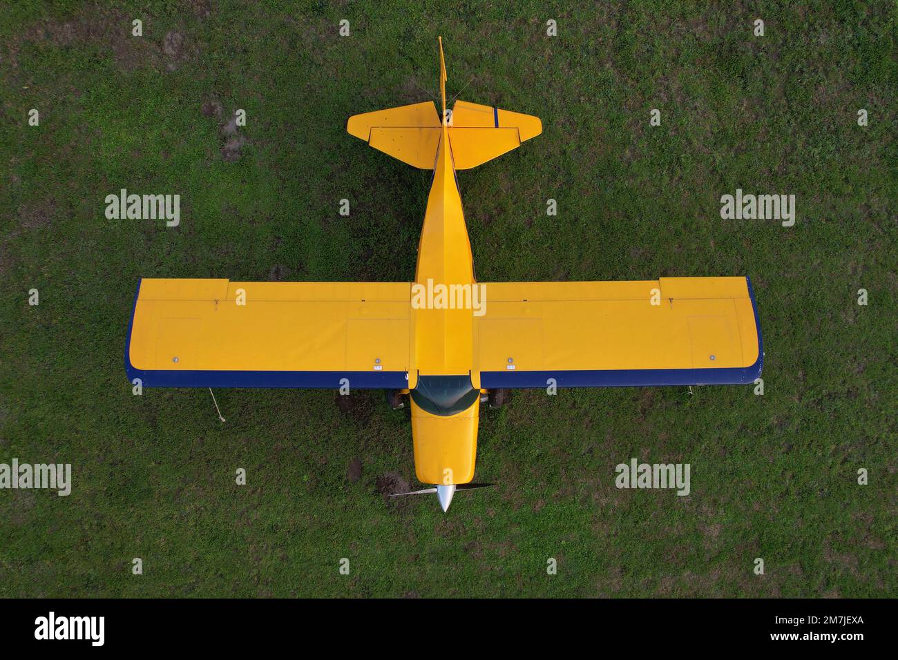 small yellow plane used for short trips seen from above parked on a green field Stock Photo