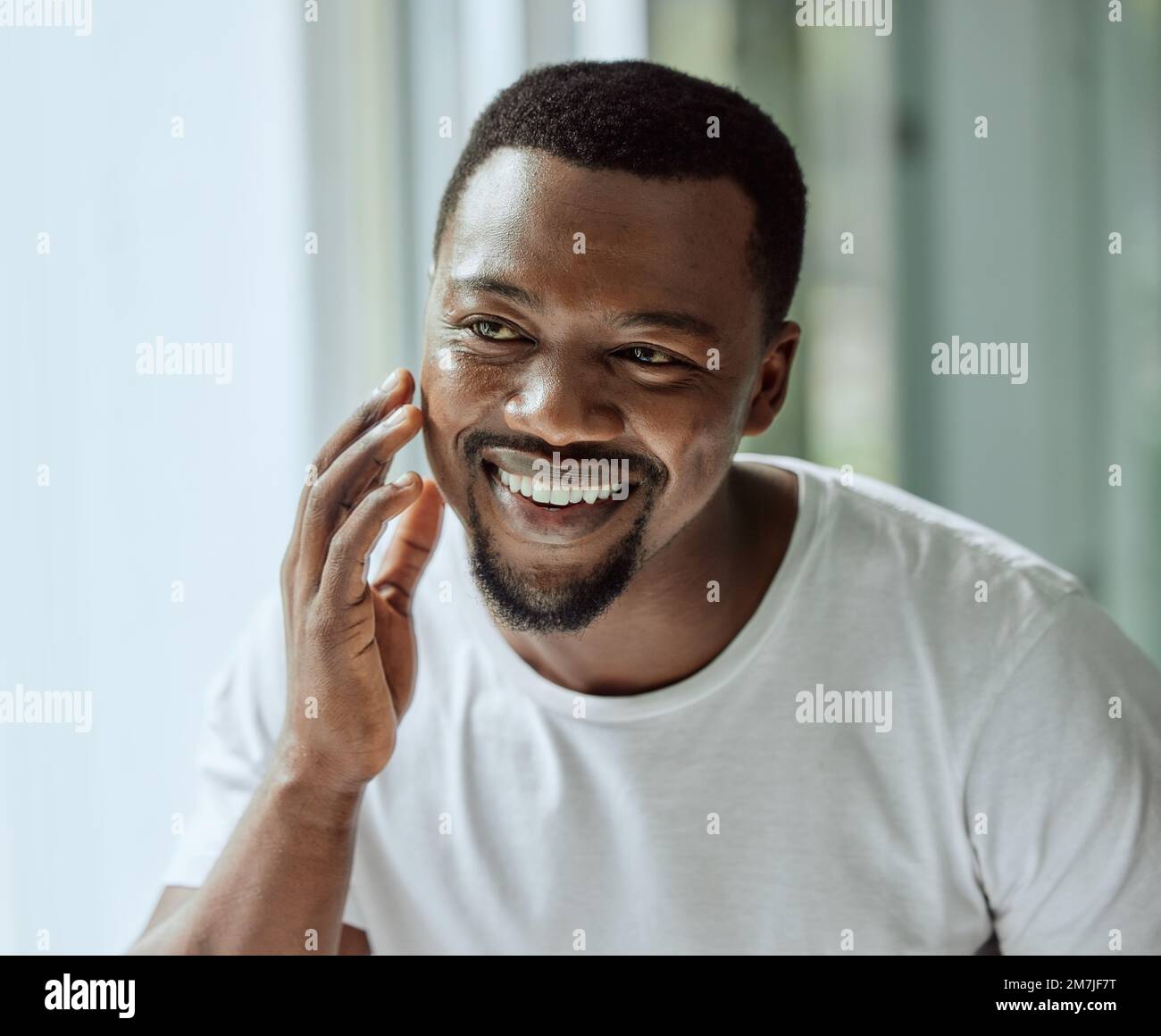 Face, antiaging and skin with a black man looking in the bathroom mirror during his morning routine at home. Skincare, beauty and reflection with a Stock Photo