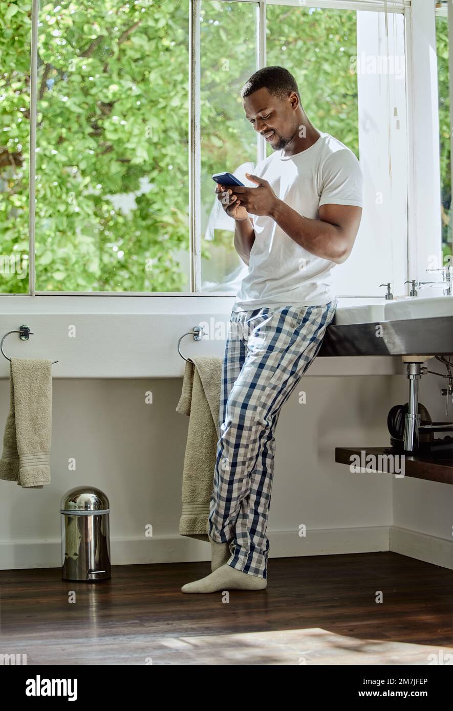 Home, phone and black man in bathroom on social media, texting or internet browsing. Relax, cellphone or happy male holding mobile smartphone for web Stock Photo