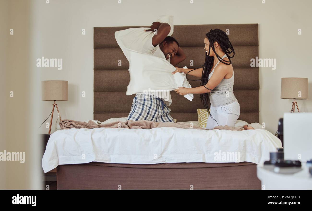 Love, pillow fighting and play with a black couple having fun in the bedroom of their home tofether in the morning. Dating, playful and joking with a Stock Photo