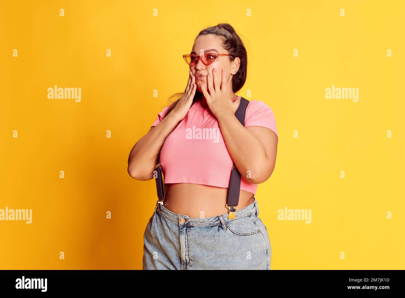 Portrait of young overweight woman in casual bright clothes posing over vivid yellow studio background. Beauty Stock Photo