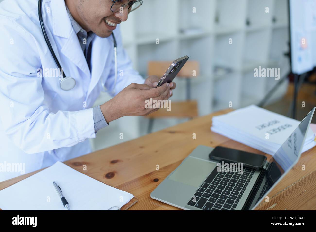 Portrait of a doctor looking at a patient's information before treating a disease with using smart phone and computer in work Stock Photo