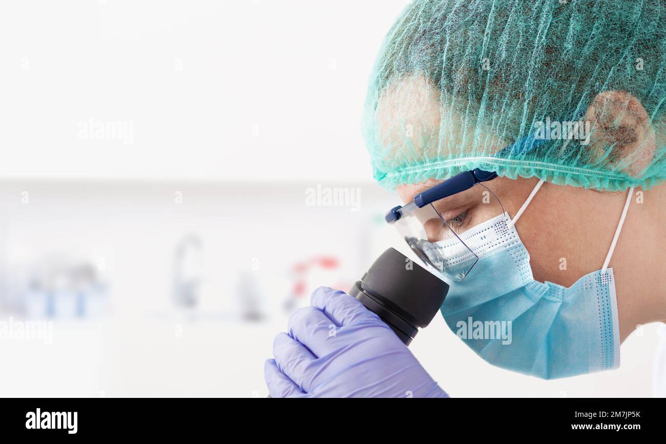 Shot of a cheerful young female scientist looking through the lens of a microscope while being seated inside of a laboratory witch copy space. Stock Photo