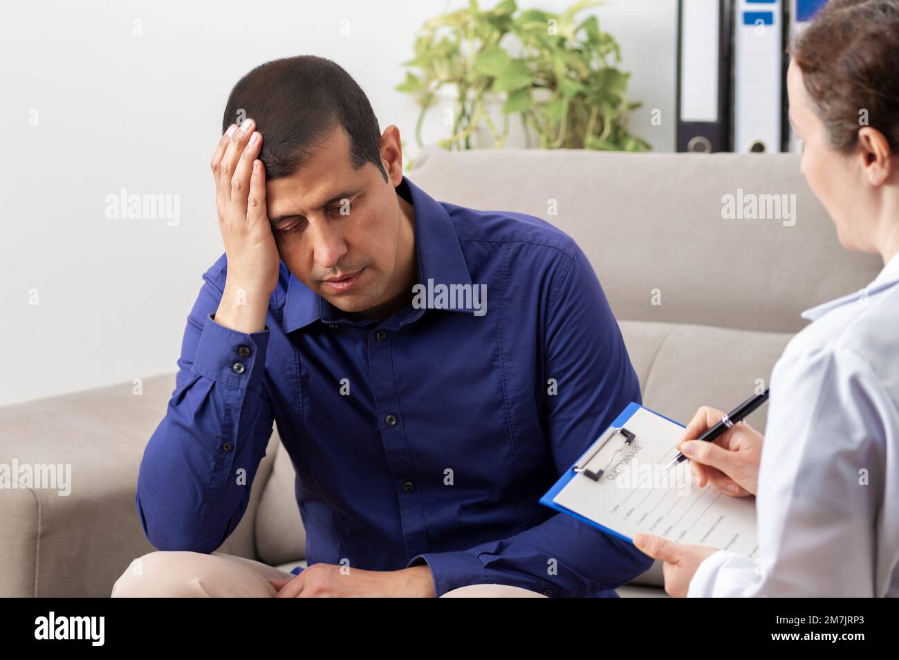 Distraught businessman holds his head in his hands while speaking to a healthcare professional. Stock Photo