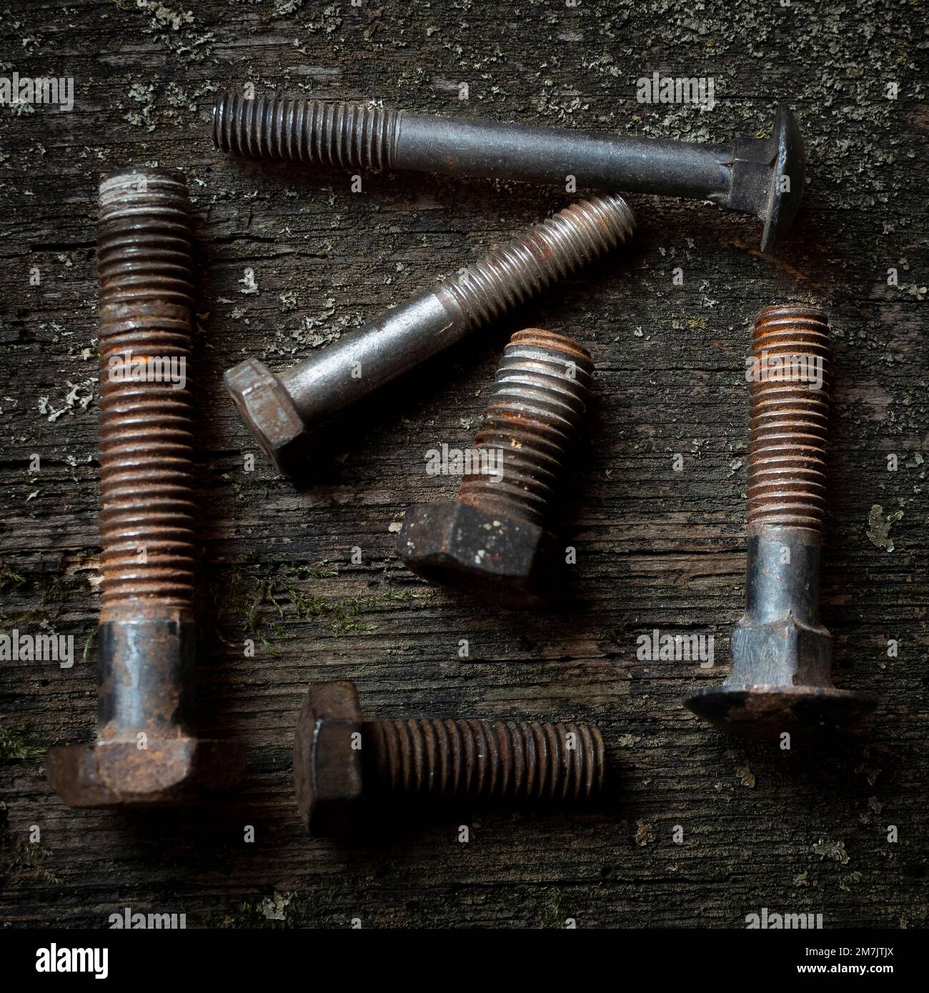 A collection of various rusted bolts and screws on a wooden surface in a workshop setting Stock Photo