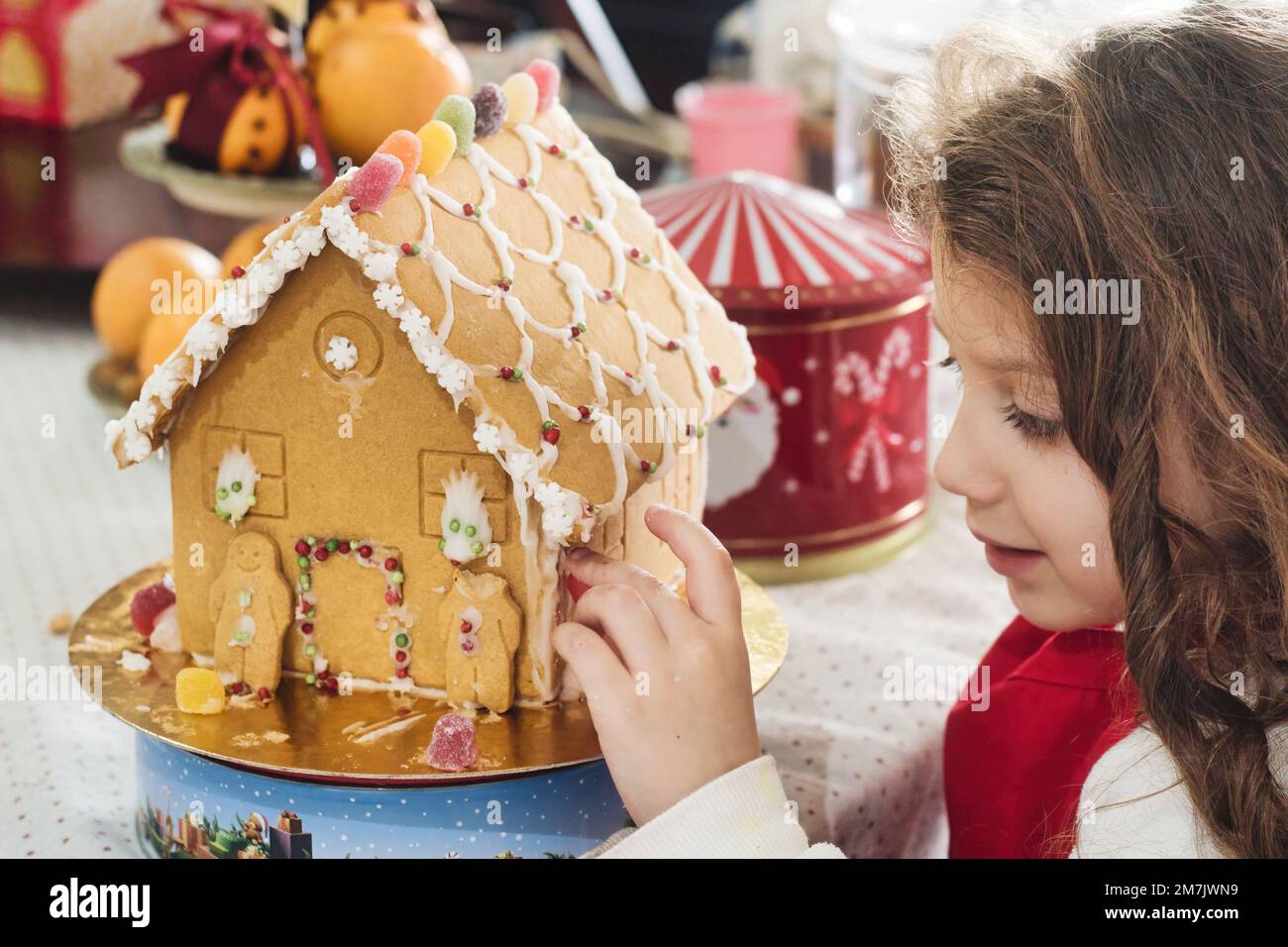 A young white Caucasian girl putting the finishing touches to a homemade gingerbread house Stock Photo