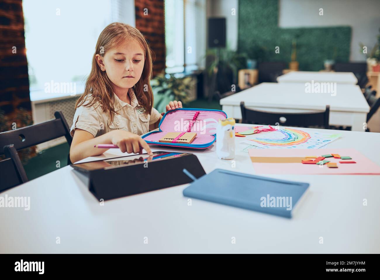 Schoolgirl using tablet. Child doing homework sitting at desk in ...