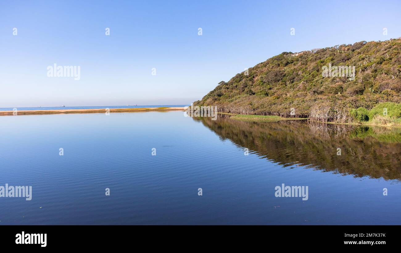 Tropical beach river lagoon mirror smooth water reflecting of headland trees vegetation landscape on a summers day. Stock Photo
