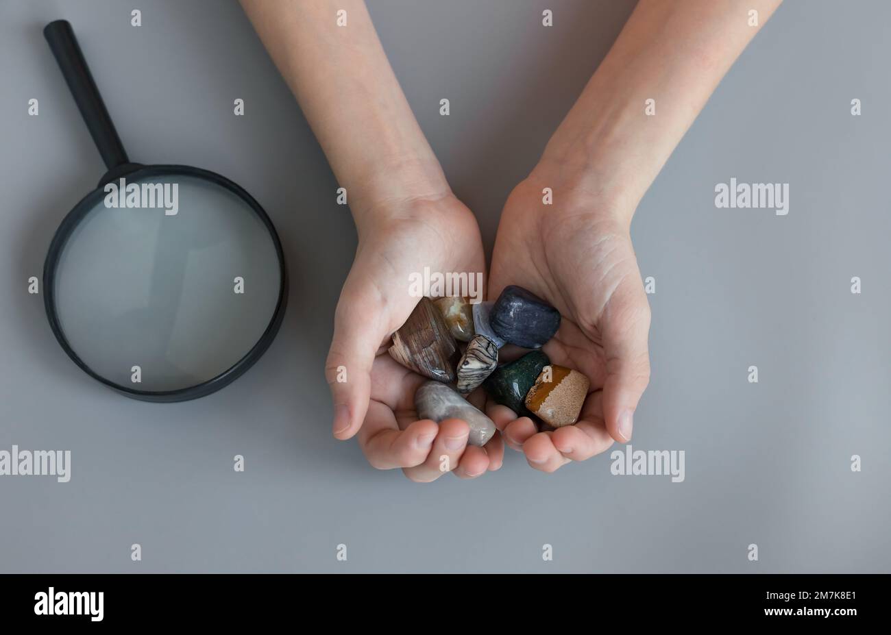 child holding collection of various semiprecious stones in hands on gray desk Stock Photo