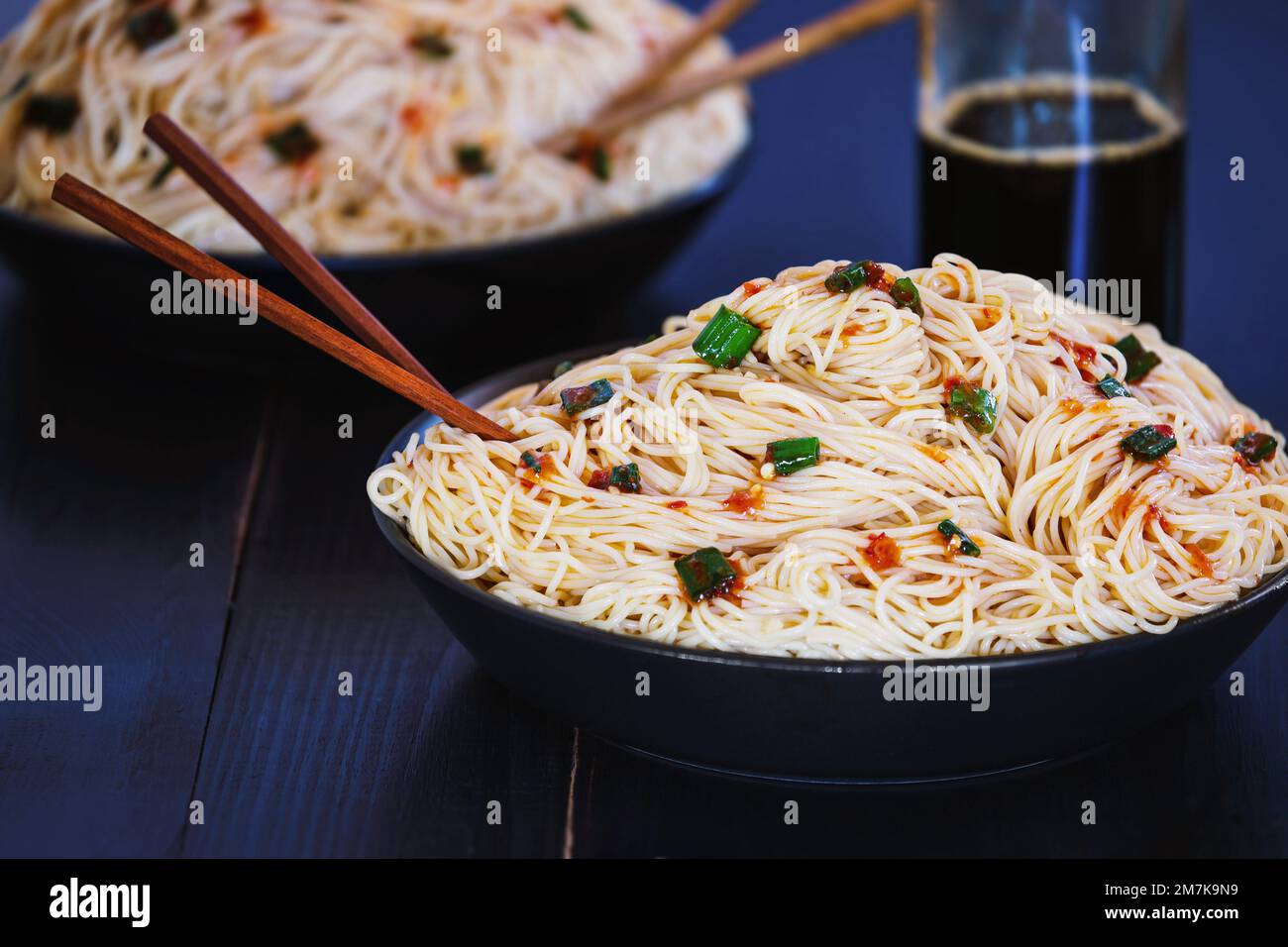 Selective focus of two bowls of vegetarian Asian Chinese noodles over a black rustic wood table with blurred foreground and background. Stock Photo