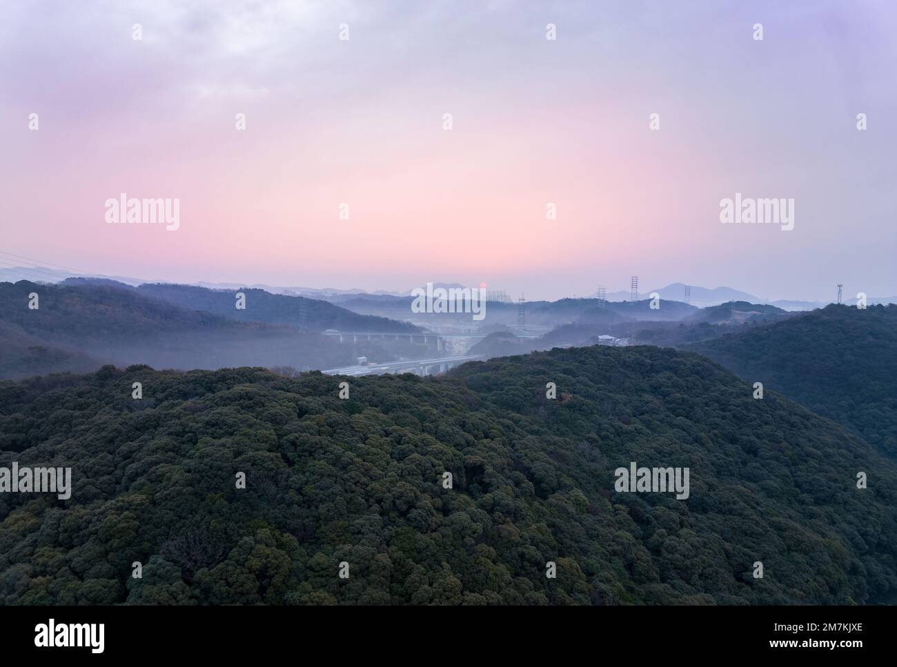 Distant early morning sun lights sky pink over misty hilly landscape Stock Photo