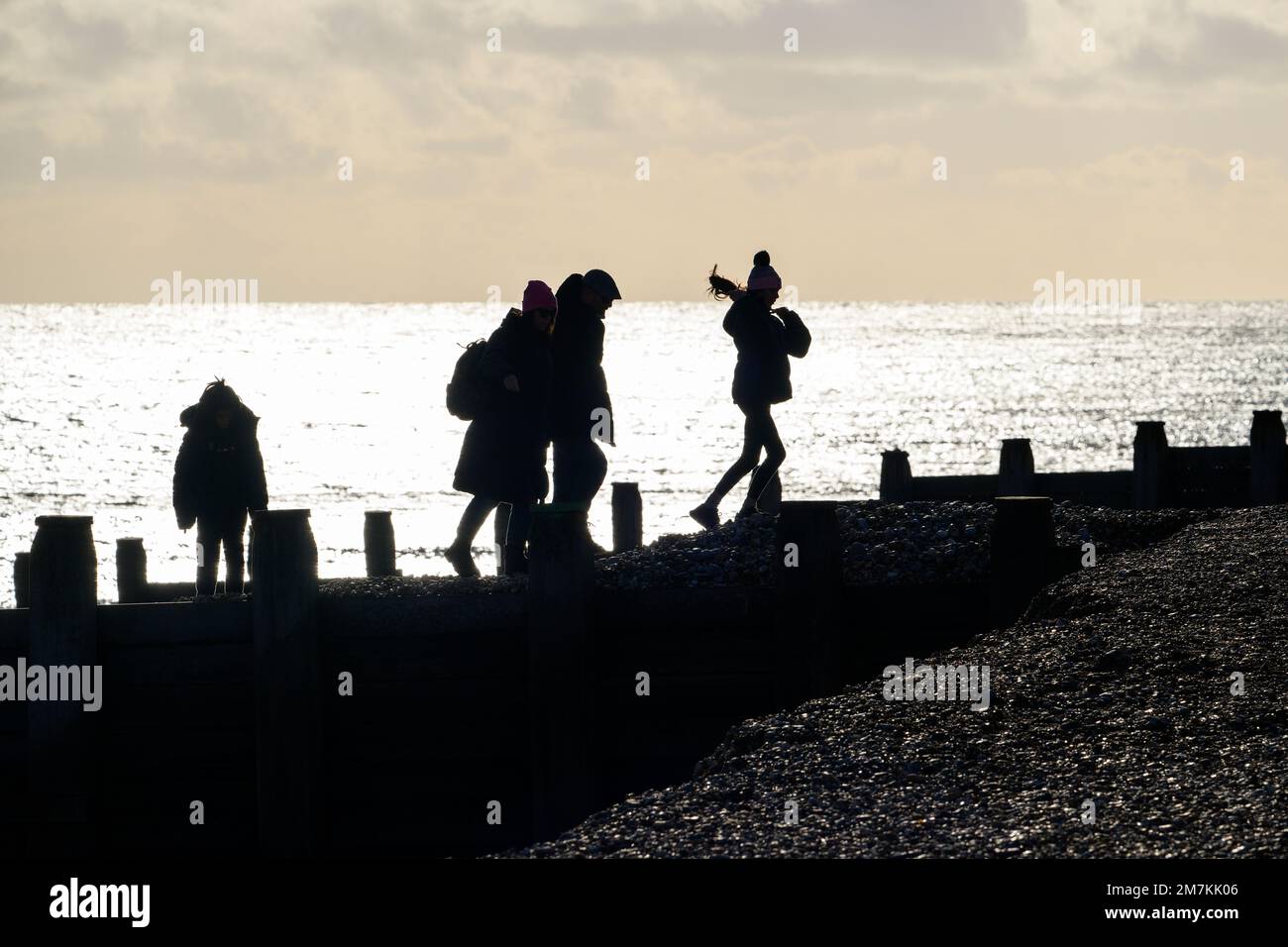 A silhouette of a family walking on Eastbourne beach, wrapped up warm for the winter sunshine. Stock Photo