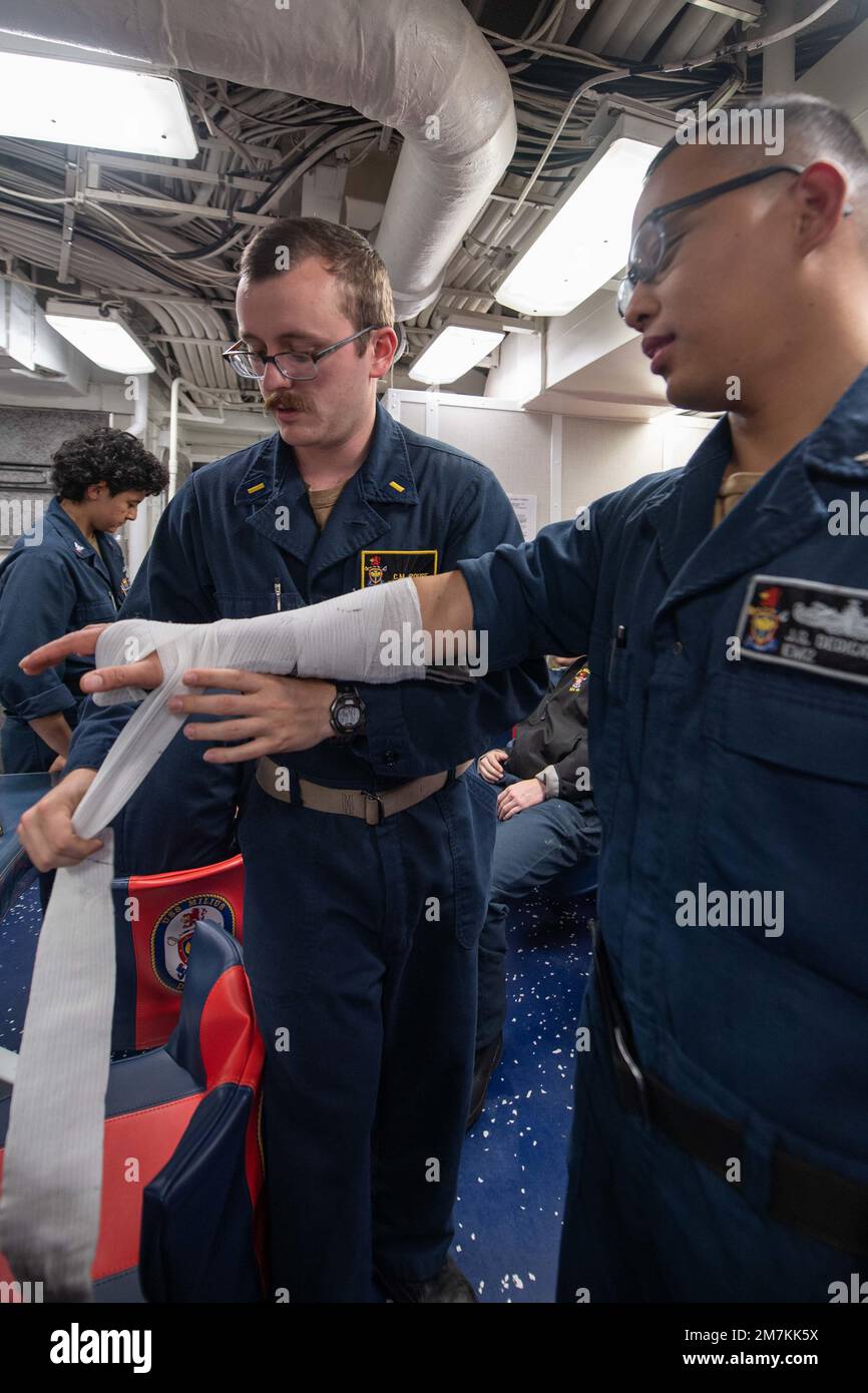 PACIFIC OCEAN (May 10, 2022) Ens. Cameron Rouse, from Raleigh, N.C., practices the application of a splint on Electrician’s Mate 2nd Class Jerome Dedicatoria, from San Diego, during tactical combat casualty care training in the mess decks aboard the Arleigh Burke-class guided missile destroyer USS Milius (DDG 69). Milius is currently conducting routine operations in the U.S. 7th Fleet area of responsibility. Stock Photo