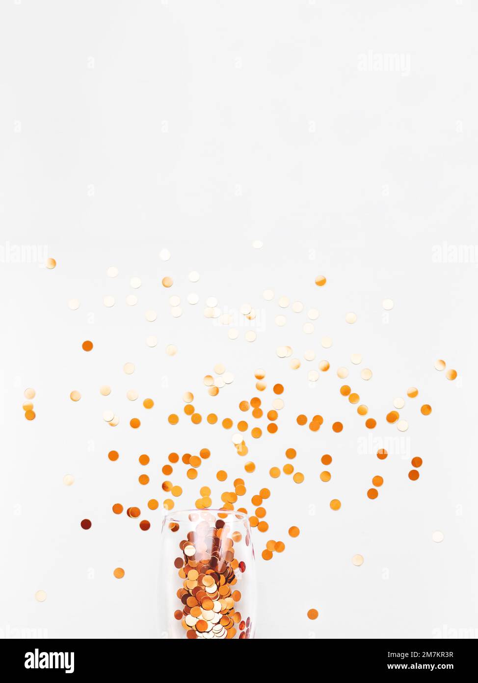 Top view on transparent wine glass with exploded firework of golden spangles. Festive copy space with crockery on white background. Stock Photo