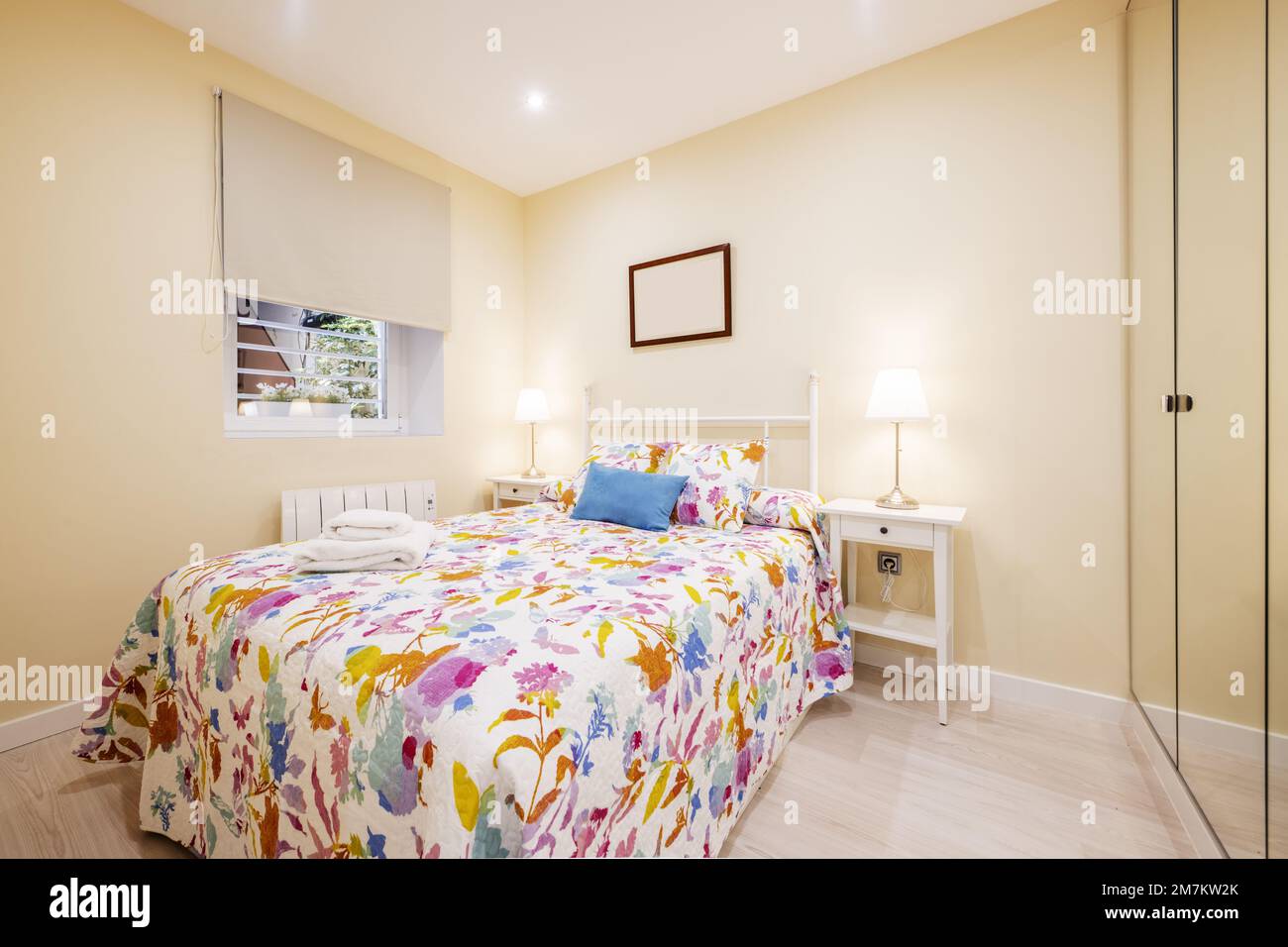 Bedroom with double bed and lined wall with built-in wardrobe with mirror doors and colorful patterned bedspread Stock Photo