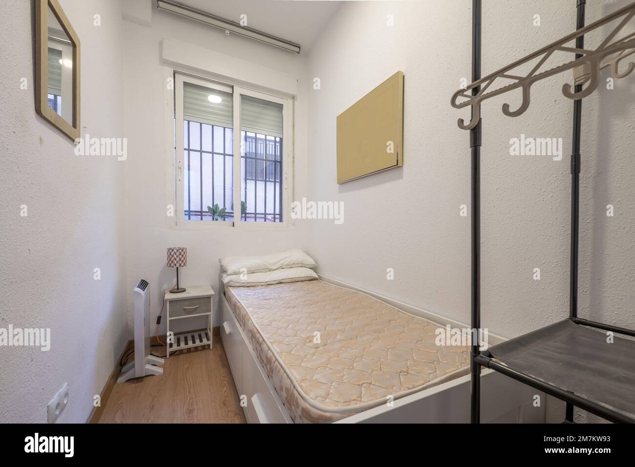 Bedroom with single bed with barred aluminum window and open wardrobe