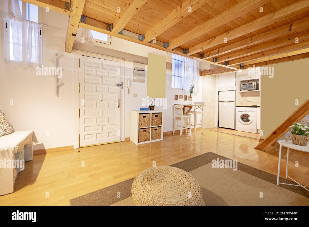 A pine wood paneled loft apartment with white furniture on the ground floor with a paneled access door and parquet floors with a beige rug and small o Stock Photo