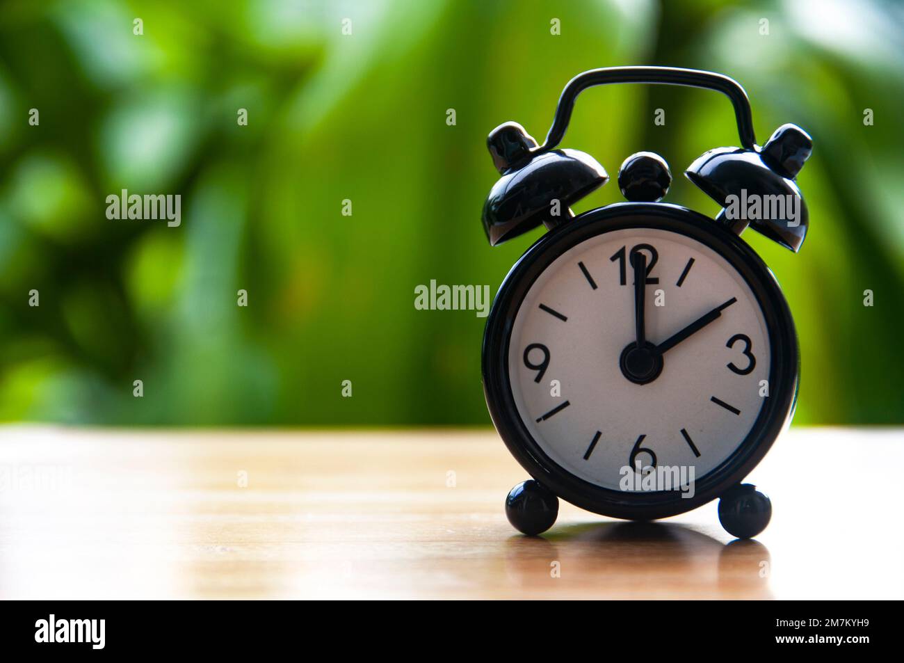 Alarm clock pointing at 2pm with blurred nature background. With customizable space for text. Copy space. Stock Photo