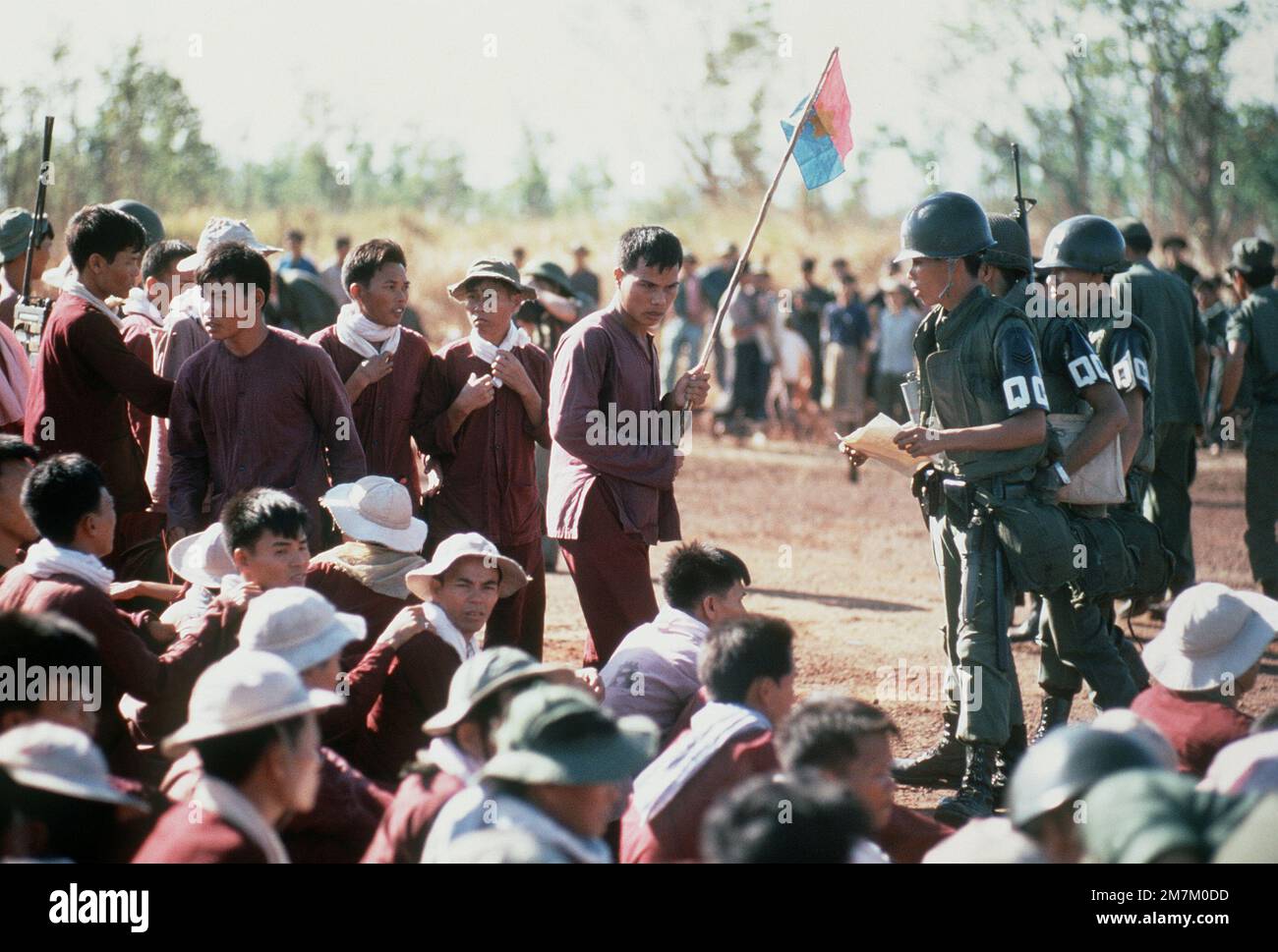 Viet Cong POWs, one with a Viet Cong flag, stand and sit at the exchange location. They were flown in on USAF C-130 aircraft from Bien Hoa Air Base. They will be exchanged for American and South Vietnamese POWs held by the Viet Cong forces. Subject Operation/Series: HOMECOMING Base: Loc Ninh Country: South Vietnam Stock Photo