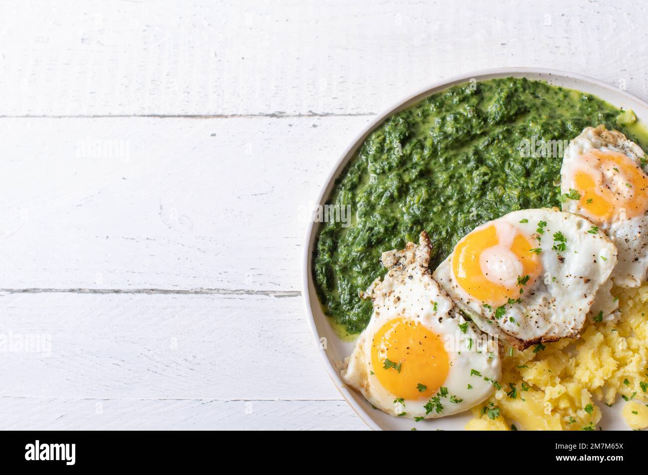 Creamy spinach with fried eggs and potatoes on a plate isolated on white background with space for text. Flat lay Stock Photo