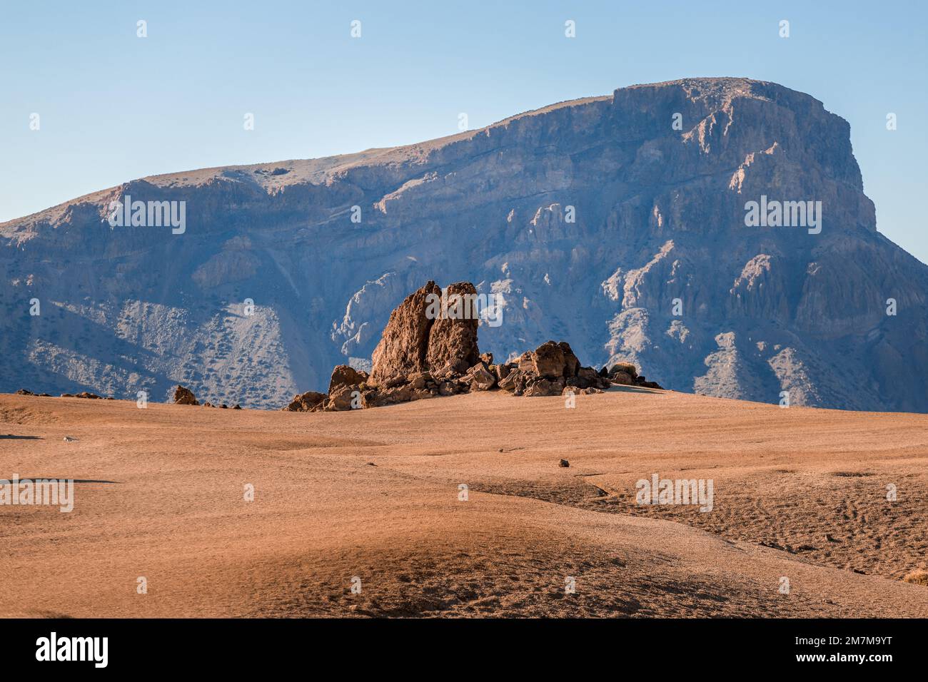 Empty orange sandy field with rocks in the background, resembling the landscape of Mars, beneath a clear blue morning sky Stock Photo