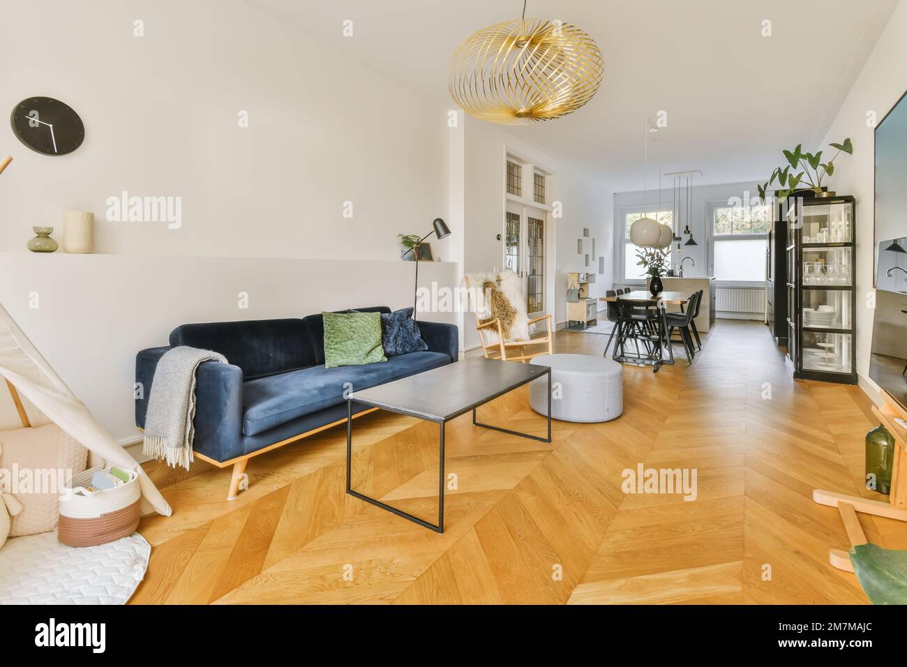 a living room with wood flooring and white walls in the center of the room is a blue velvet sofa Stock Photo