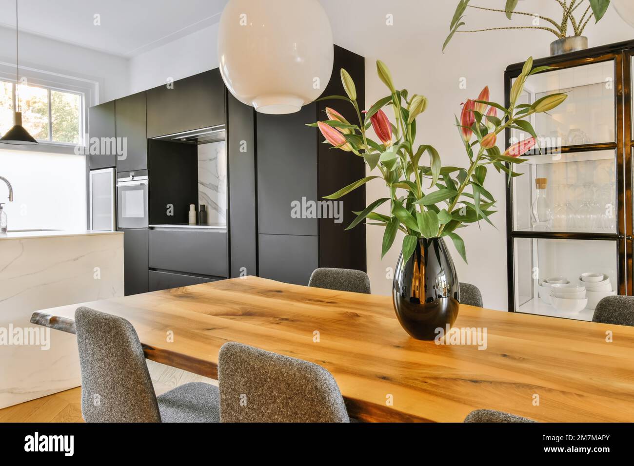 a kitchen and dining area in a modern home with white walls, black cabinets and wooden table surrounded by grey chairs Stock Photo