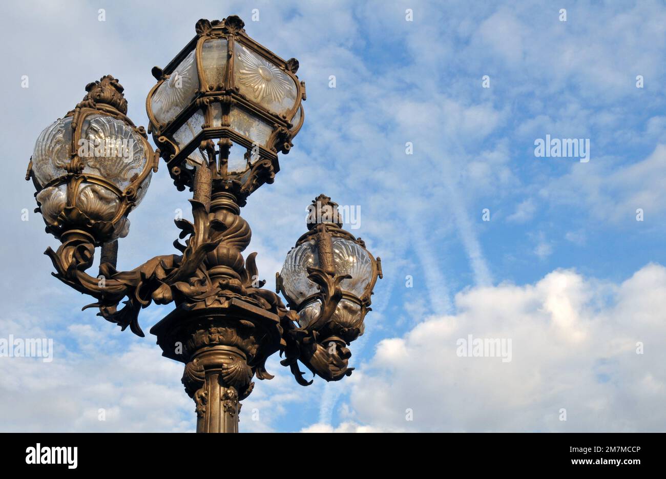An ornate Art Nouveau street lamp on the landmark Pont Alexandre III bridge against a partly cloudy sky in Paris. Stock Photo