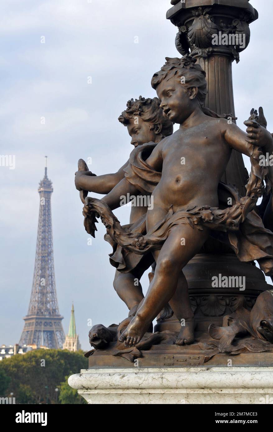 The Eiffel Tower stands in the background behind bronze sculptures at the base of a lamp on the Pont Alexandre III bridge in Paris. Stock Photo