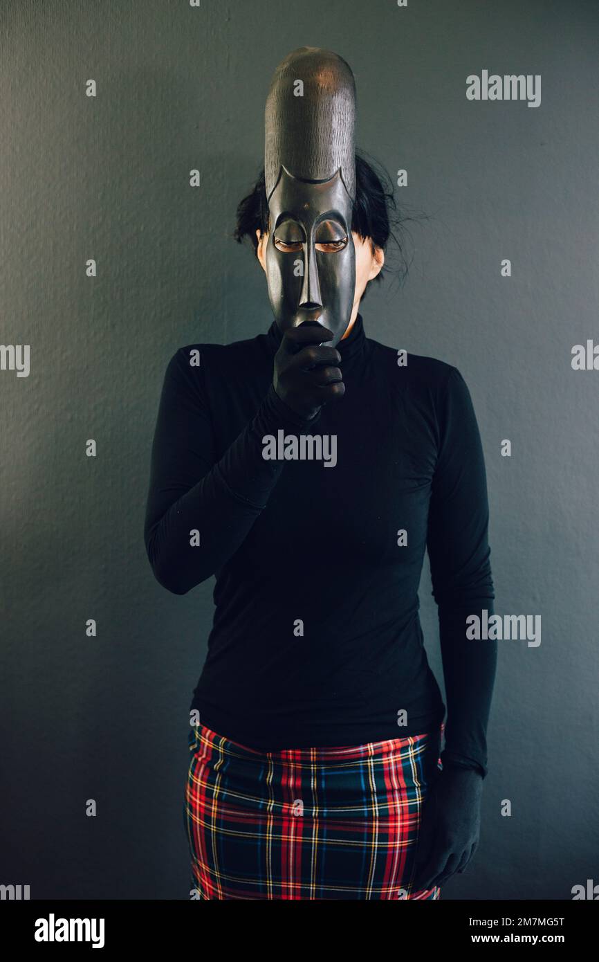 Black haired woman with an African mask in front of her face Stock Photo