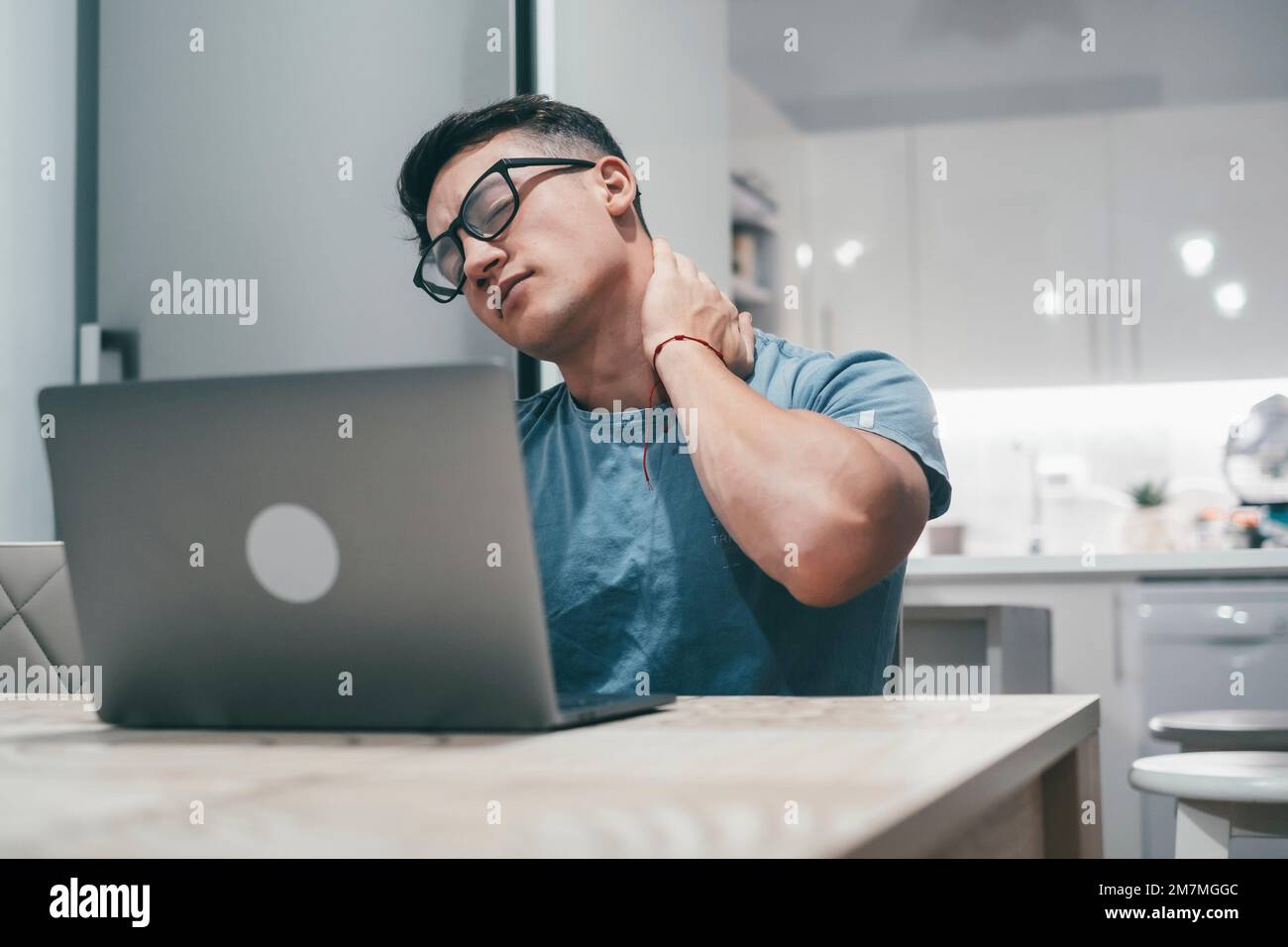 One young sick man feeling bad and pain on his neck muscle at home after overwork with laptop. Teenager with physical problems working at night. Stock Photo