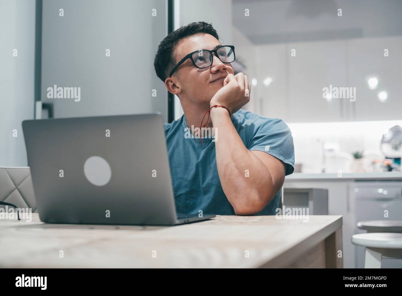 One young happy boy using computer working and having fun alone at home looking up dreaming and thinking and enjoying. Teenager man with glasses working and studying Stock Photo