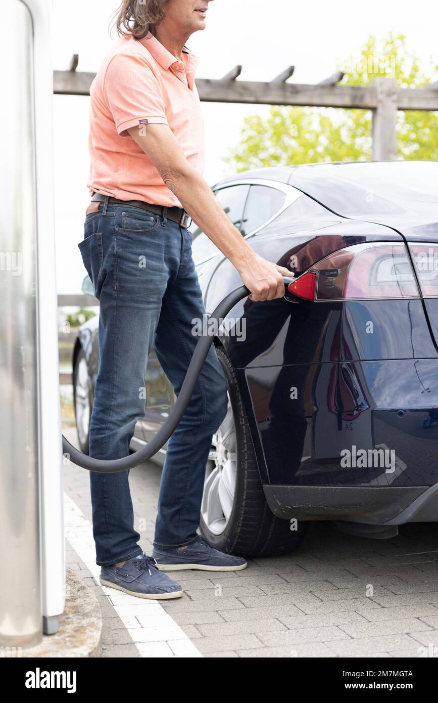 Man charges his tesla at a charging station in germany hires stock