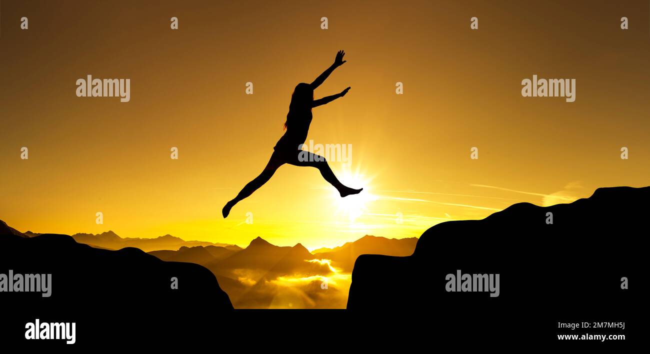 Silhouette of woman jumping over cliff Stock Photo