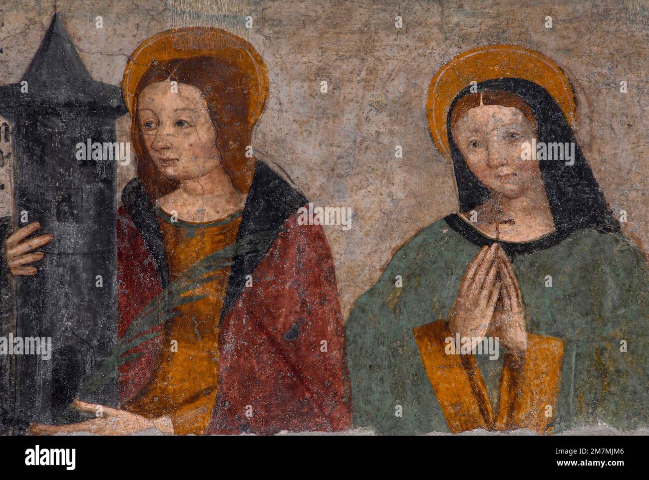 Saint Barbara (left) and Saint Margherita or Margaret of Cortona depicted in damaged Renaissance fresco, painted in 1512, on west front of deconsecrated Cappella di San Grato (Chapel of St Gratus) in Via Jean-Baptiste De Tillier in the historic centre of Aosta, regional capital of the Valle d’Aosta in northwest Italy.  Saint Barbara holds a three-windowed tower.  The tower symbolises Barbara’s imprisonment by her father.  The three windows - which she ordered be inserted in her prison - symbolise the Holy Trinity. Stock Photo