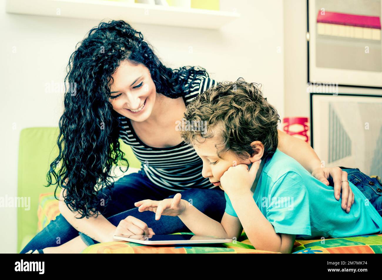 Young mother having fun with son using tablet on bed Learning computer tech with sister in