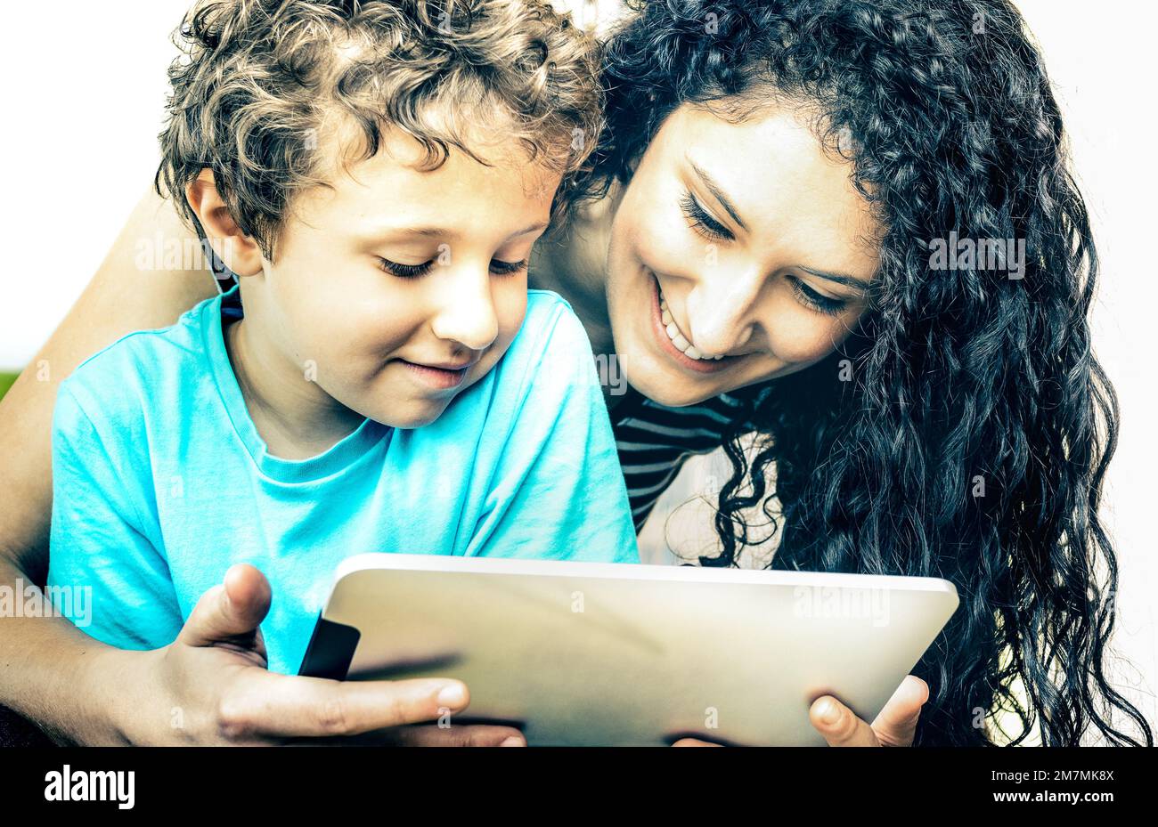Young mother having fun with son using tablet on bed Learning computer tech with sister in