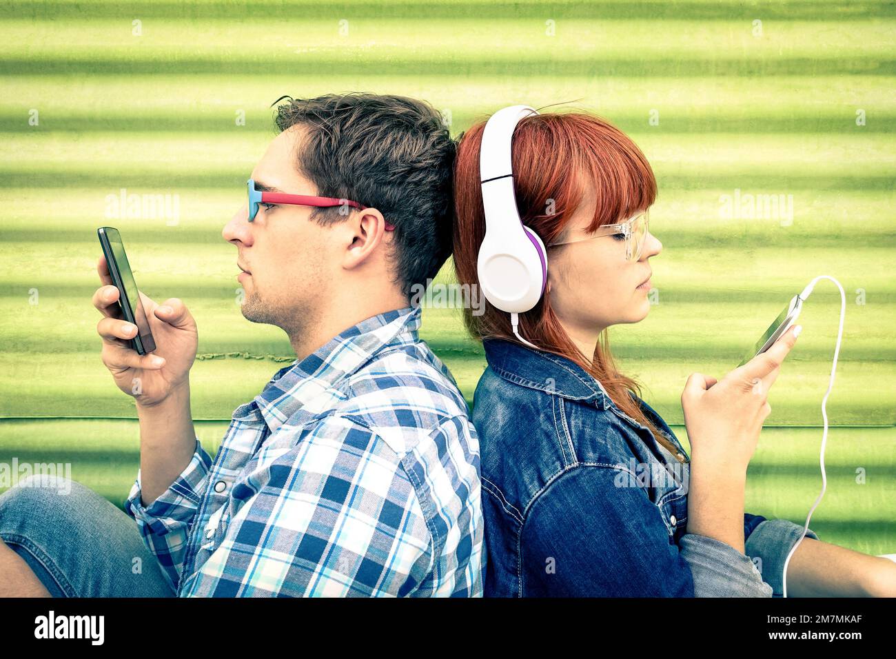 Hipster couple in disinterest moment with mobile phones - Concept of apathy sadness and isolation using new technologies - Boyfriend and girlfriend wi Stock Photo