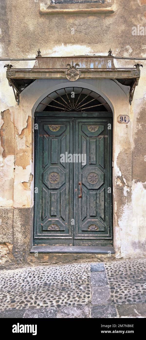 dark green double-leaf front door with canopy made of sheet metal, in an alley with cobblestones in Cefalu, Sicily Stock Photo