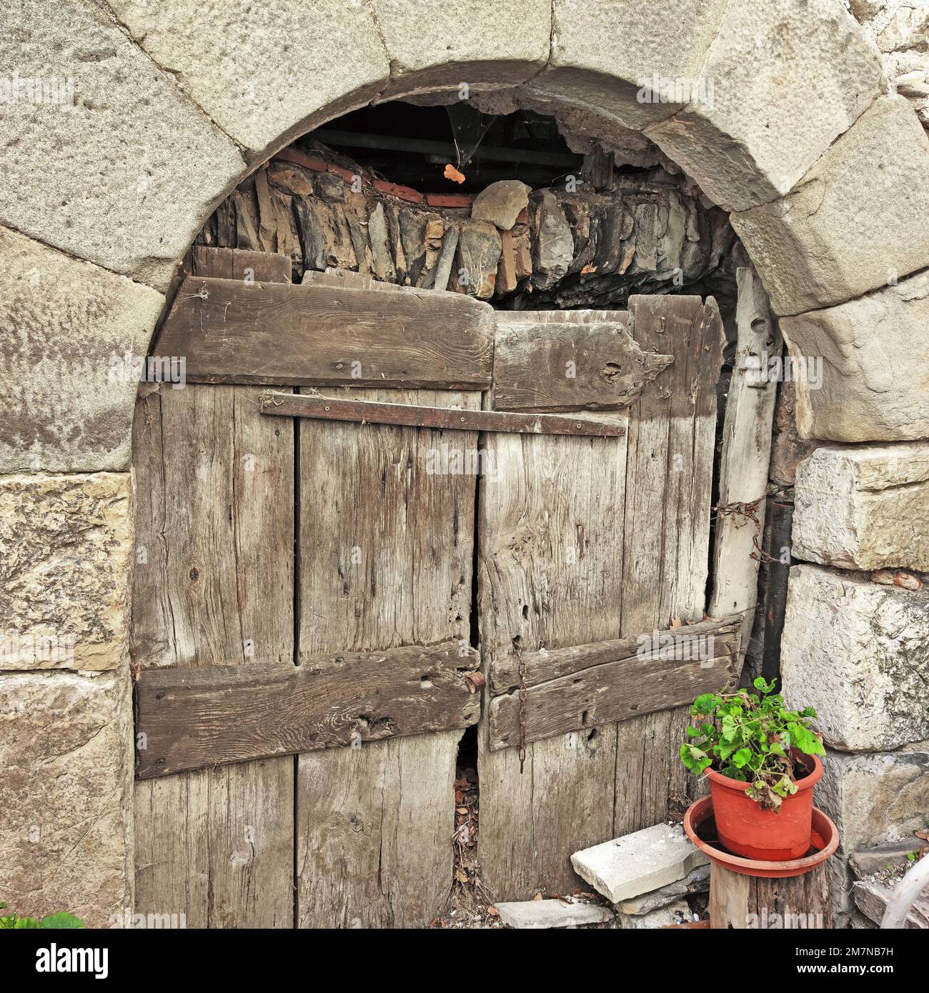 massive archway with primitive board door hides the dilapidation of a house in northern Tuscany Stock Photo