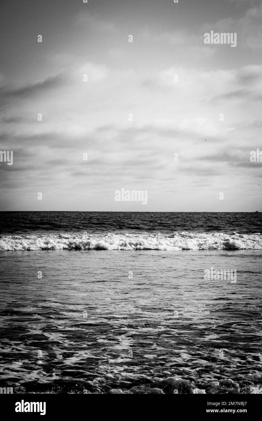 A vertical black and white shot of foamy waves of a sea under the ...