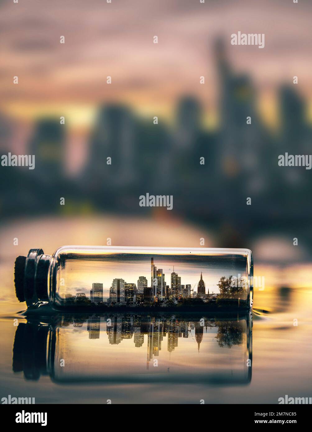 Frankfurt in a small bottle, the bottle is reflected in a puddle with the skyline in it. the skyline in the background in bokeh. evening at sunset Stock Photo