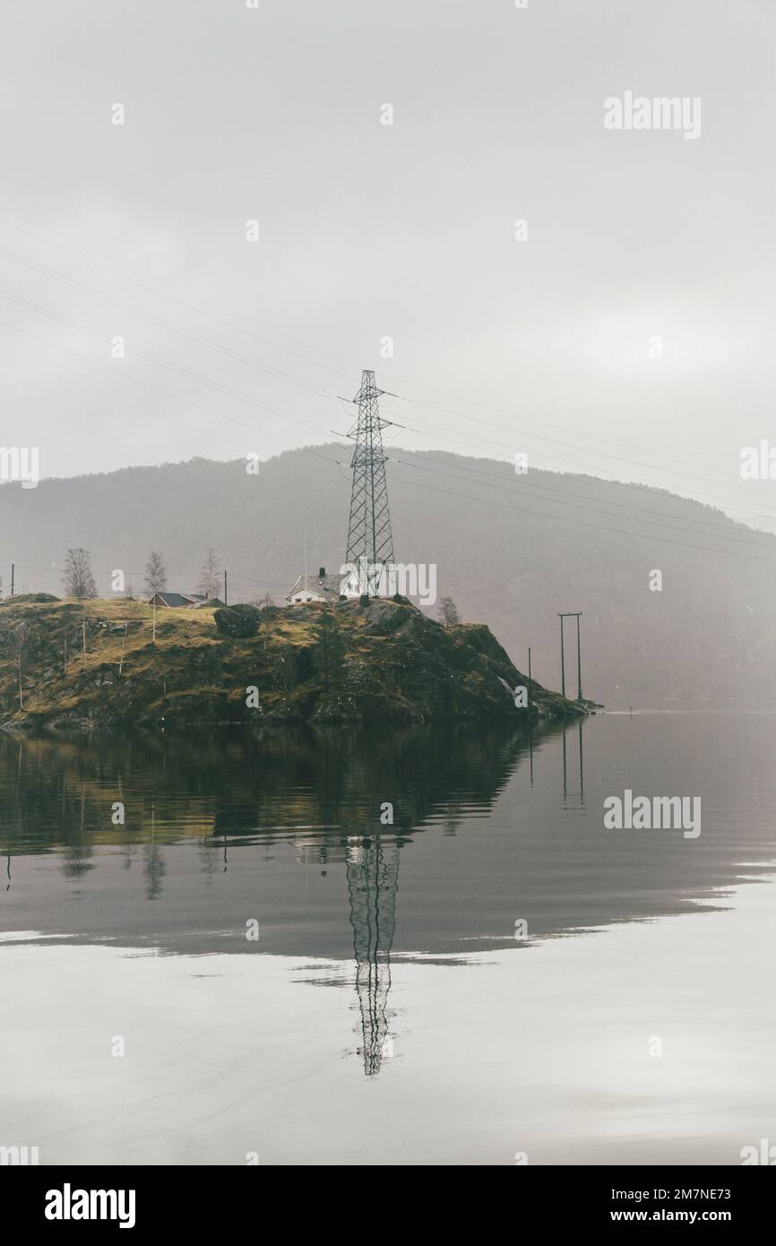 Lonely house on island with big power pole in Norway, landscape with reflection in water, typical fjord landscape with small islands, isolation from outside world Stock Photo