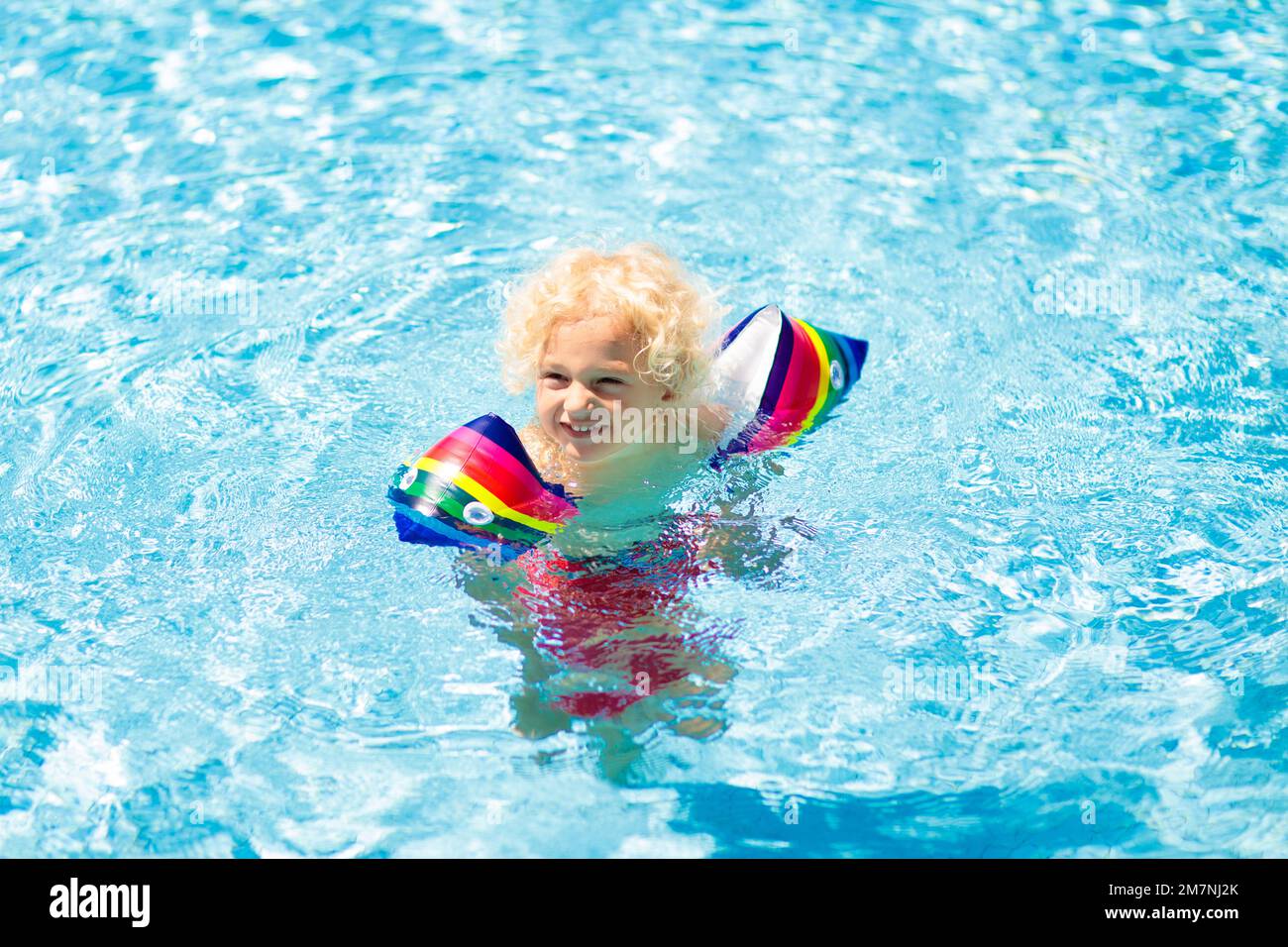 Child in swimming pool wearing colorful inflatable armbands. Kids learn