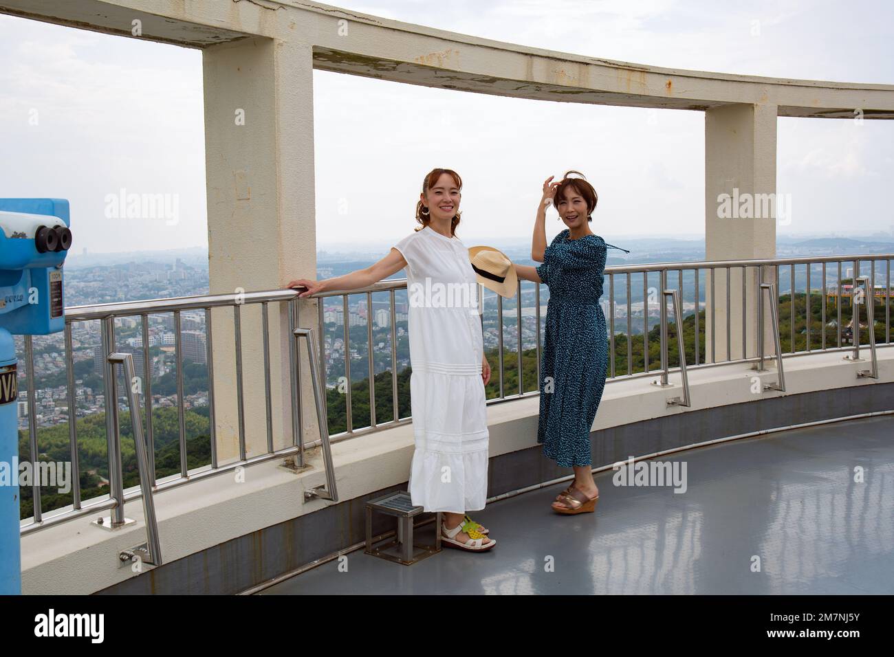 Two mature Japanese women at a viewing platform outdoors in summer, leaning on the rail. Stock Photo