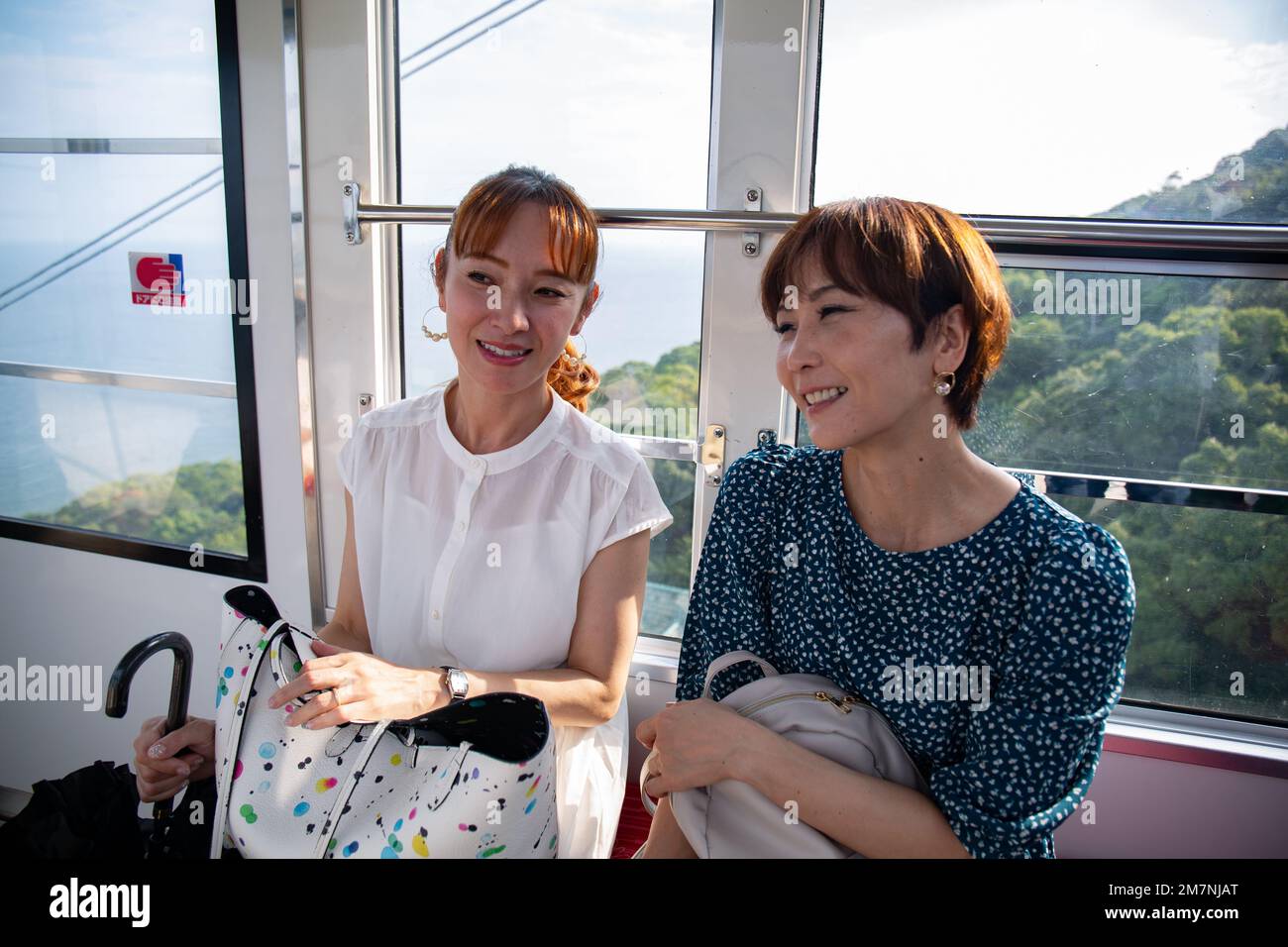 Two mature women seated side by side in a cable car, friends on a day out. Stock Photo