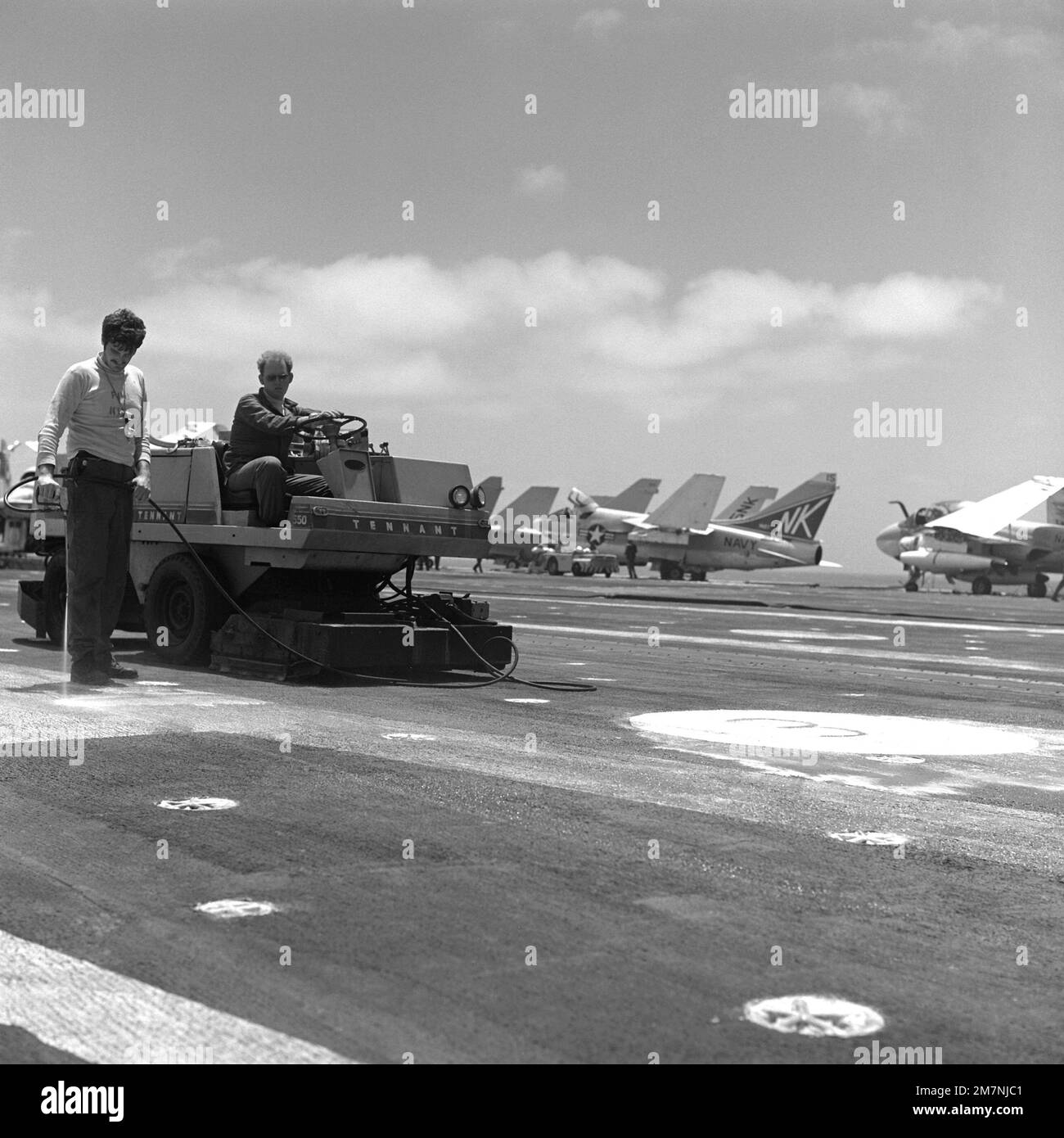 Crew members perform maintenance on the flight deck of the aircraft carrier USS CORAL SEA (CV-43). Parked in the background are A-7E Corsair II aircraft and an A-6E Intruder aircraft, right. Country: Indian Ocean (IOC) Stock Photo