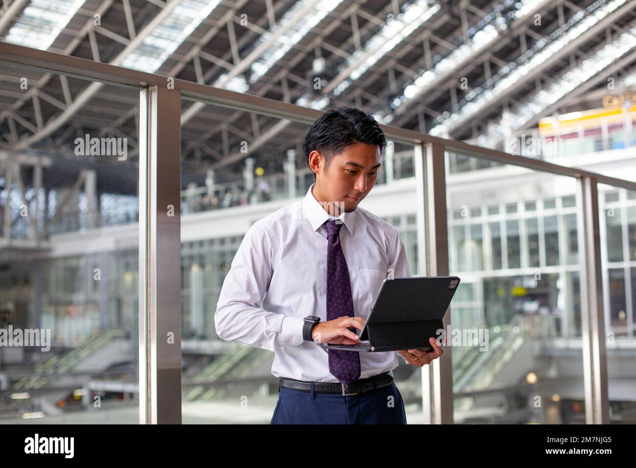 A young businessman in the city, on the move, standing on a walkway, using his laptop. Stock Photo