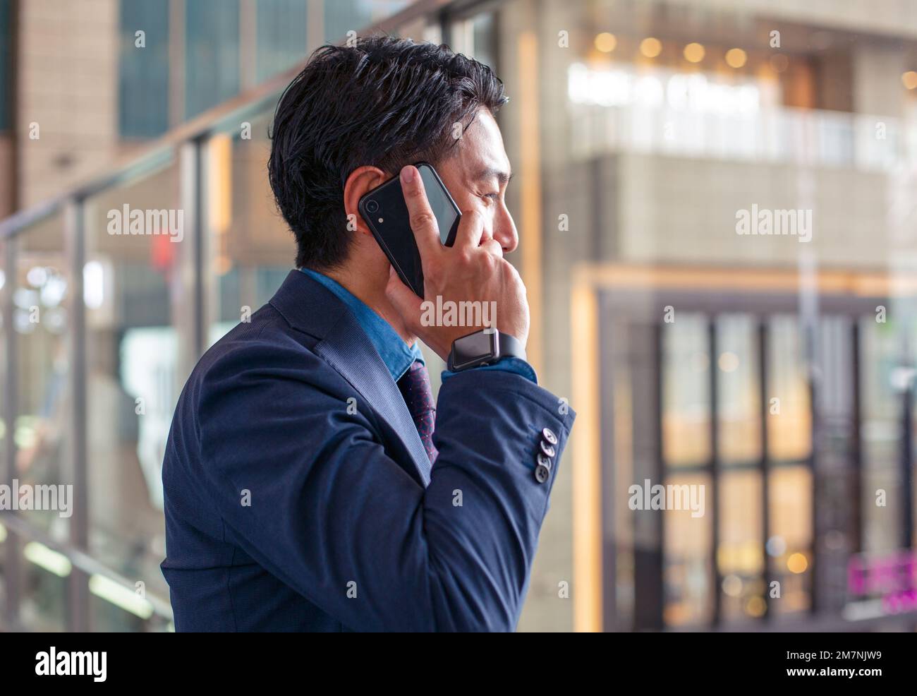 A young businessman in a blue suit on the move in a city downtown area, speaking on his mobile phone. Stock Photo